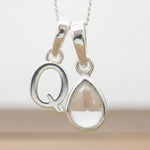 Silver Initial Q necklace with a teardrop-shaped Herkimer Quartz crystal pendant hanging above a rustic wooden surface