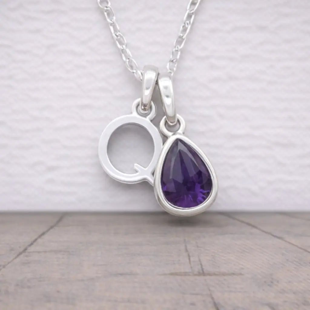 Silver initial q necklace with a purple teardrop pendant on a light wooden surface.