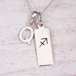 Sterling silver initial Q and Sagittarius zodiac bar necklace, close-up of the letter charm and pendant on whitewashed wood