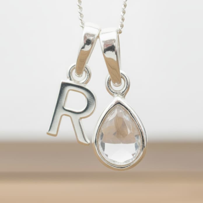 Silver Initial R necklace with a teardrop-shaped Herkimer Quartz crystal pendant hanging above a rustic wooden surface