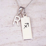Sterling silver initial R and Sagittarius zodiac bar necklace, close-up of the letter charm and pendant on whitewashed wood