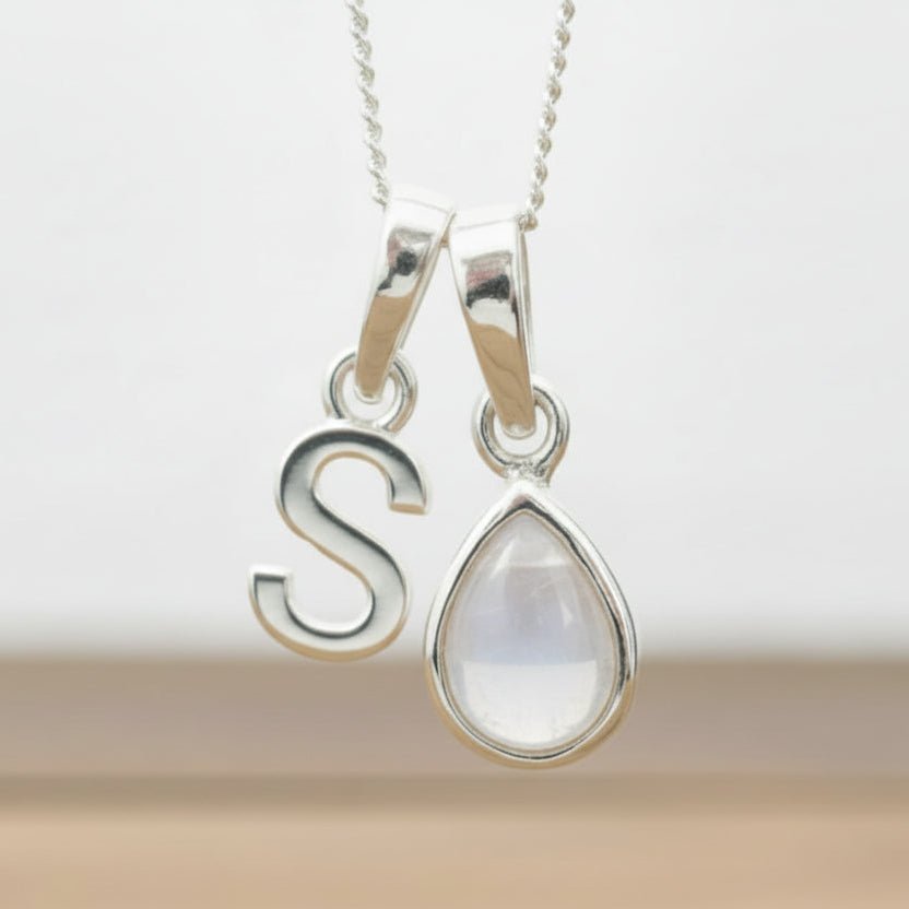 Silver Initial S necklace with a teardrop-shaped Herkimer Quartz crystal pendant hanging above a rustic wooden surface