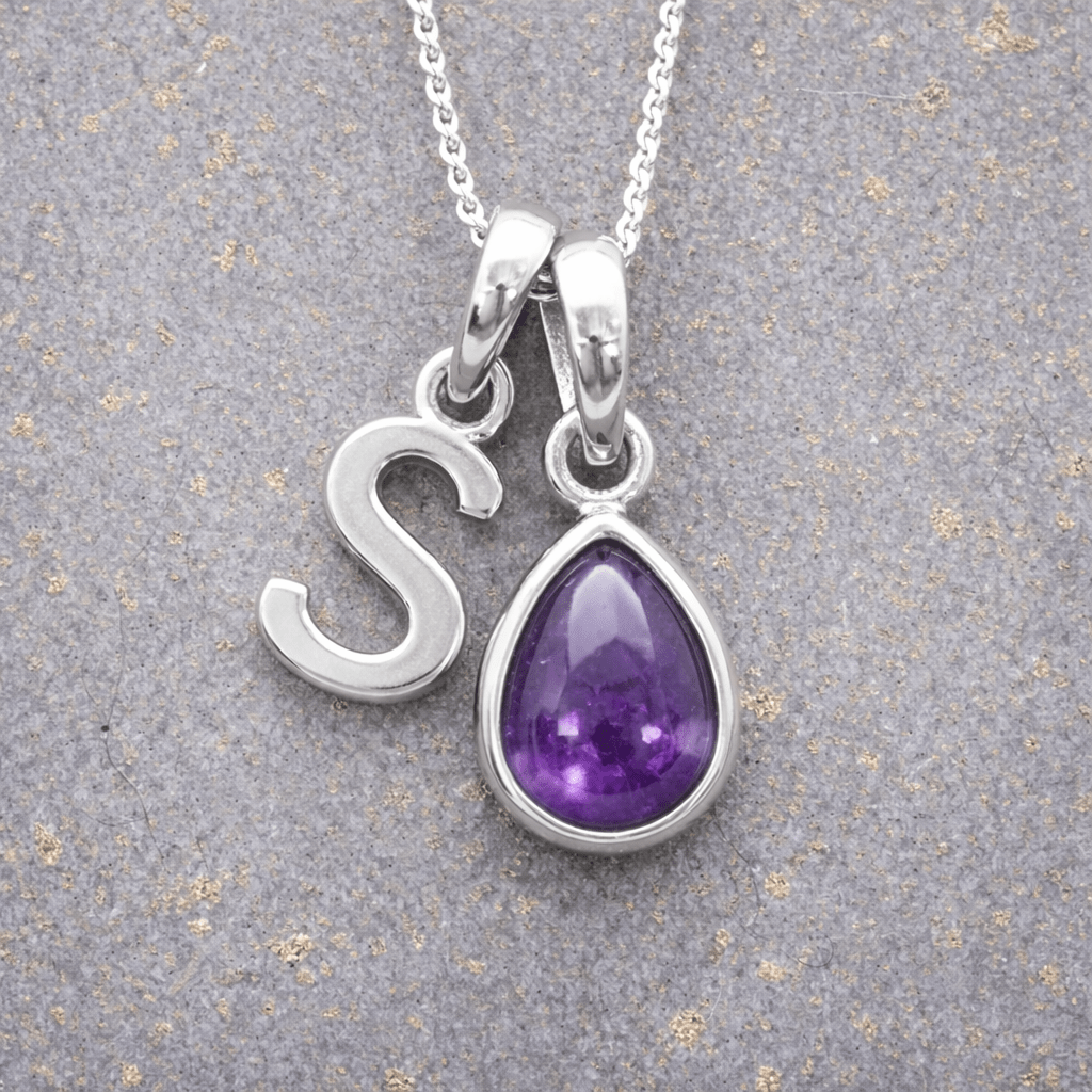 sterling Silver necklace with a 'S' initial pendant and a purple teardrop february birthstone amethyst pendant on a textured grey background