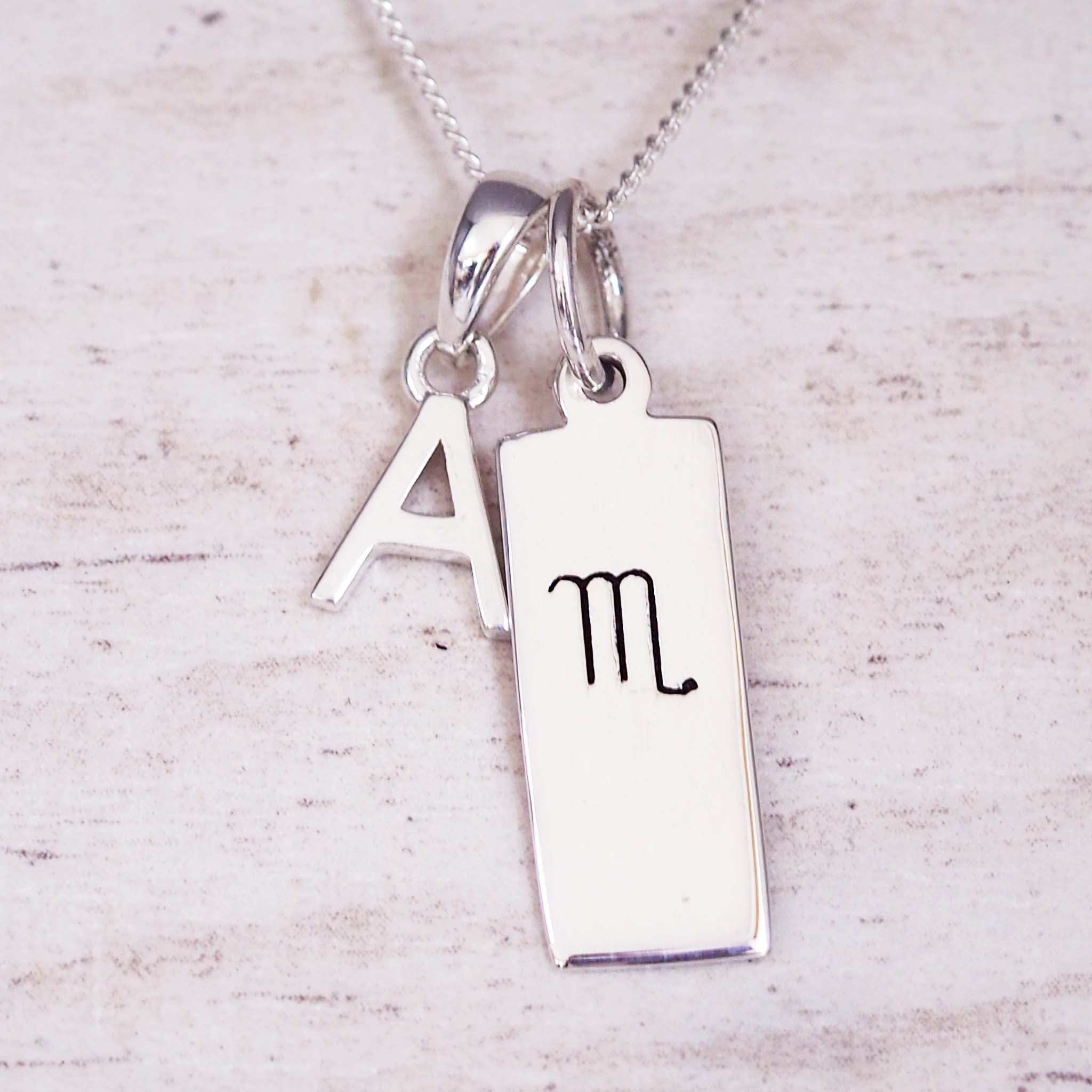 Silver necklace with 'A' and Scorpio zodiac symbol pendant on a light wooden background