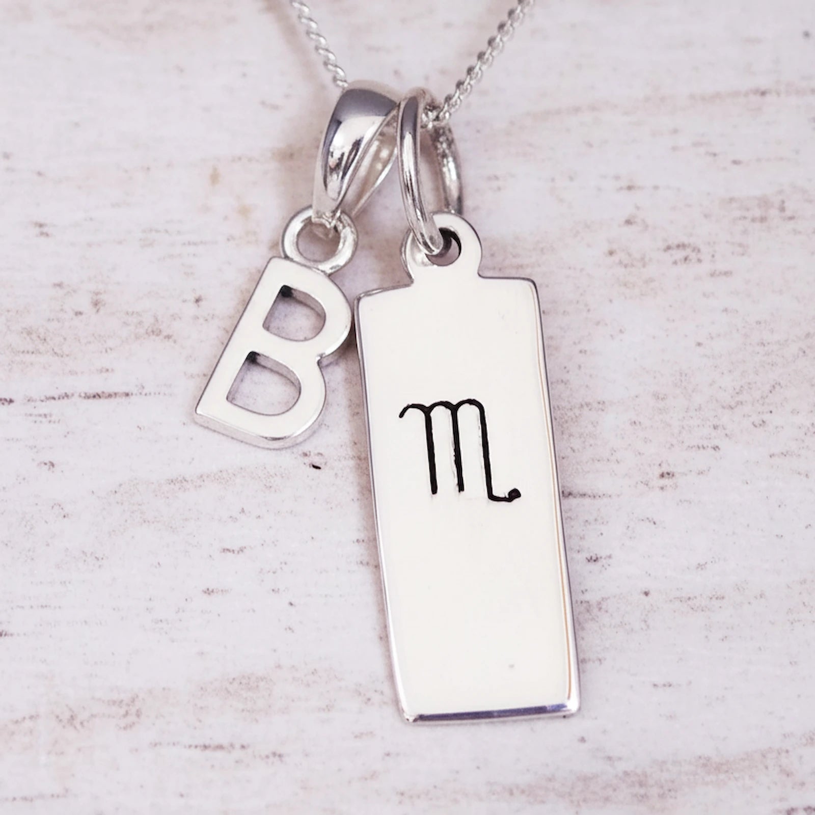 Sterling Silver necklace with 'B' initial pendant and hand drawn Scorpio zodiac symbol pendant on a light wooden background