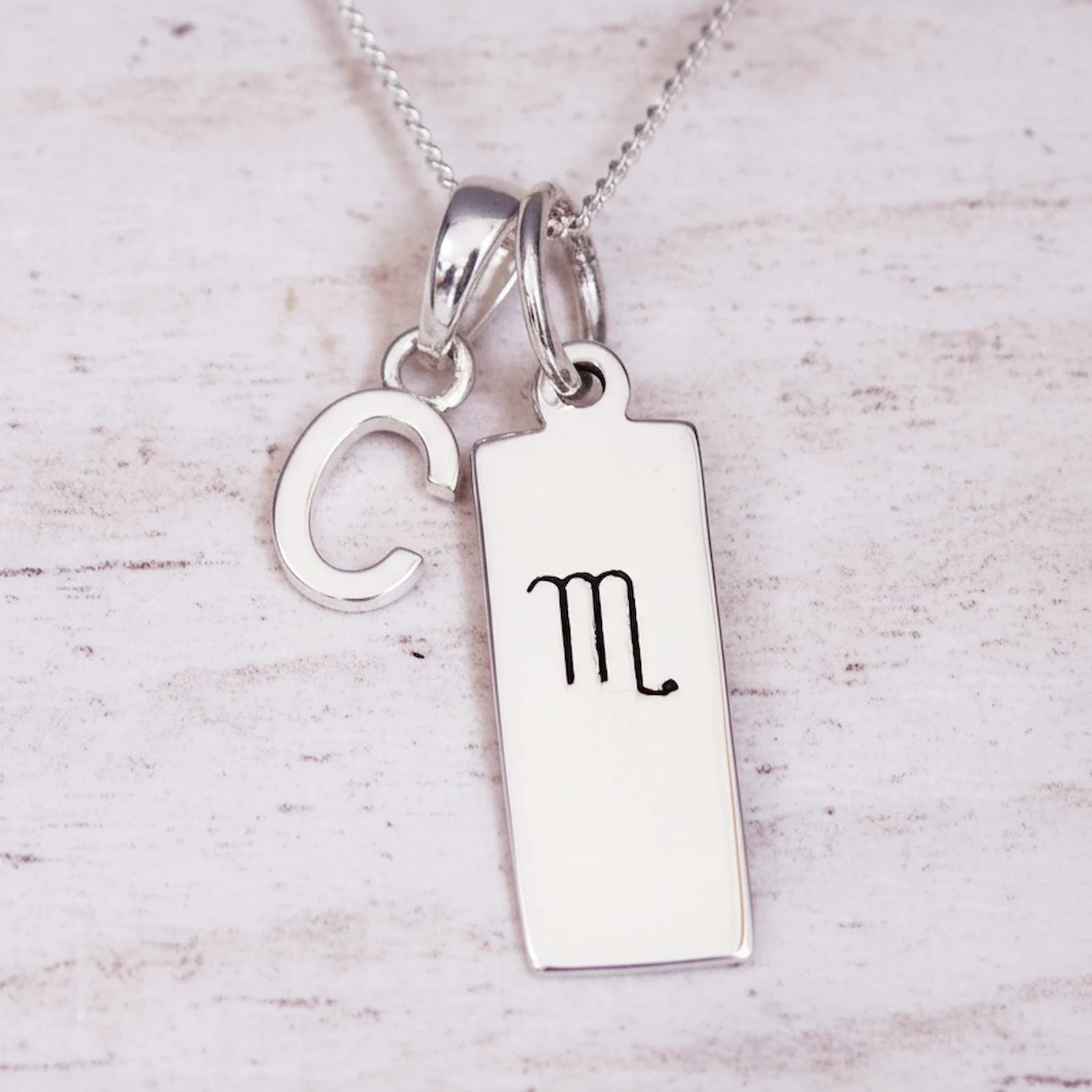 Sterling Silver necklace with 'C' initial pendant and hand drawn Scorpio zodiac symbol pendant on a light wooden background