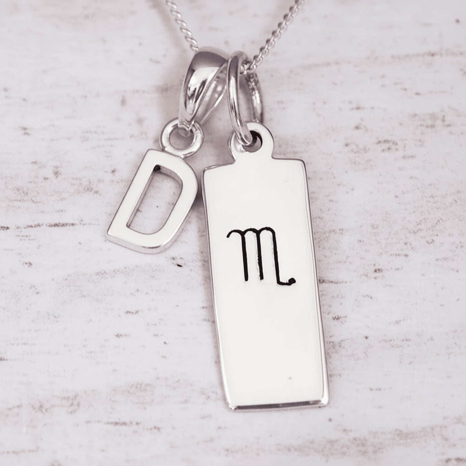Sterling Silver necklace with 'D' initial pendant and hand drawn Scorpio zodiac symbol pendant on a light wooden background