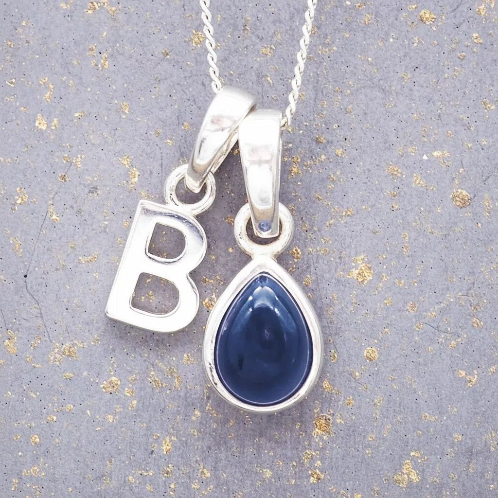 Sterling silver 'B' initial necklace with a September birthstone blue sapphire pear-shaped pendant on a grey background.