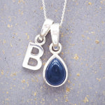 Sterling silver 'B' initial necklace with a September birthstone blue sapphire pear-shaped pendant on a grey background.