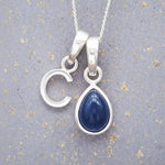 Sterling silver 'C' initial necklace with a September birthstone blue sapphire pear-shaped pendant on a grey background.