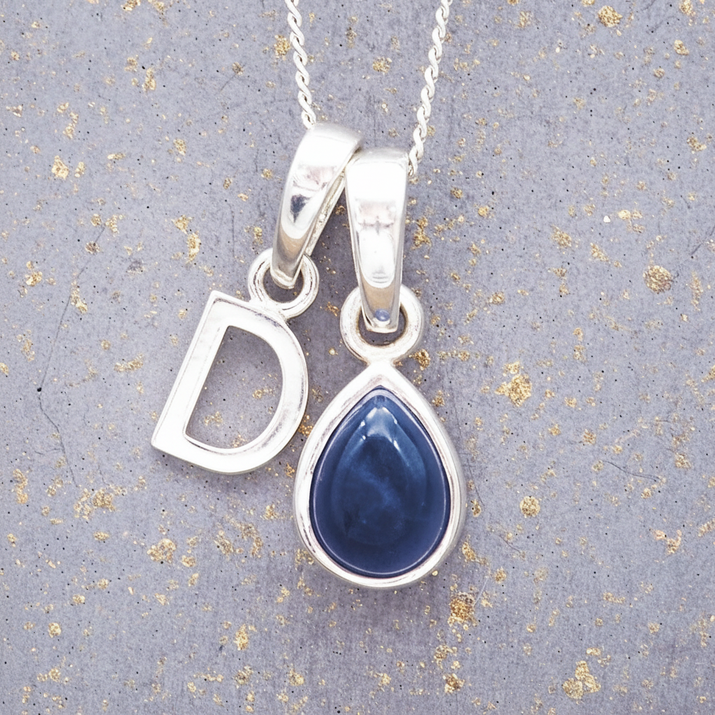 Sterling Silver necklace with a 'C' initial pendant with a blue teardrop-shaped september birthstone sapphire gemstone on a textured grey background