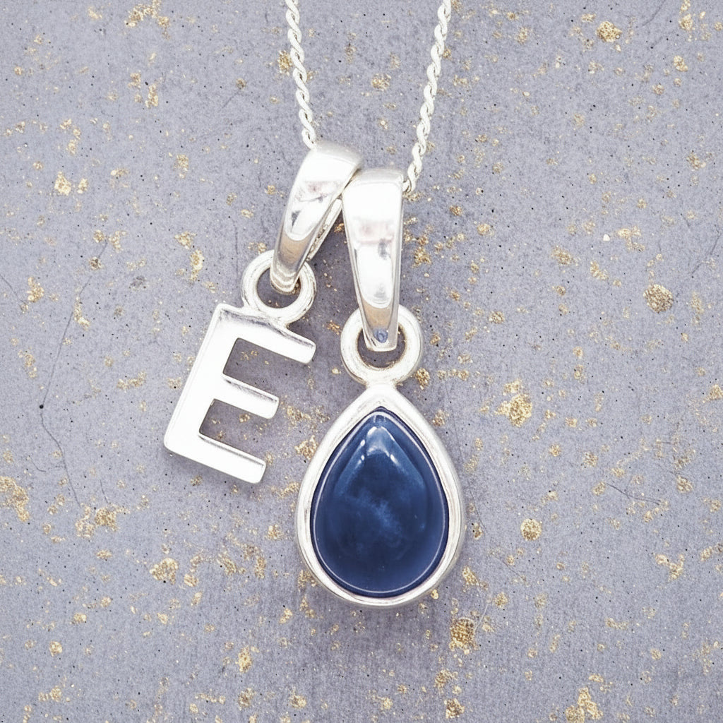Sterling Silver necklace with a 'E' initial pendant with a blue teardrop-shaped september birthstone sapphire gemstone on a textured grey background