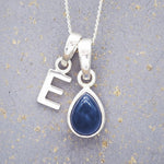 Sterling Silver necklace with a 'E' initial pendant with a blue teardrop-shaped september birthstone sapphire gemstone on a textured grey background