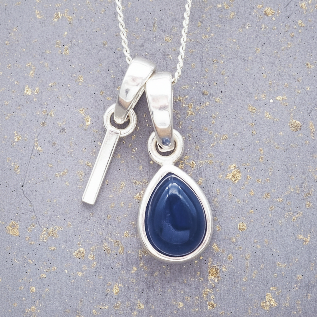 Sterling Silver necklace with a 'I' initial pendant with a blue teardrop-shaped september birthstone sapphire gemstone on a textured grey background