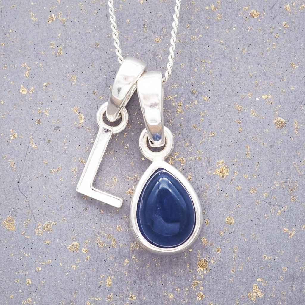 Sterling Silver necklace with a 'L' initial pendant with a blue teardrop-shaped september birthstone sapphire gemstone on a textured grey background
