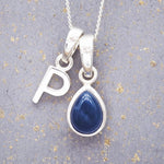 Sterling silver 'P' initial necklace with a September birthstone blue sapphire pear-shaped pendant on a grey background.