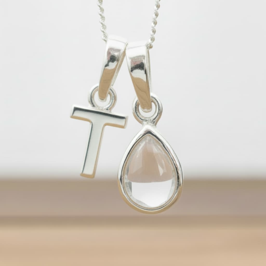 Silver Initial T necklace with a teardrop-shaped Herkimer Quartz crystal pendant hanging above a rustic wooden surface