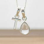 Silver Initial T necklace with a teardrop-shaped Herkimer Quartz crystal pendant hanging above a rustic wooden surface