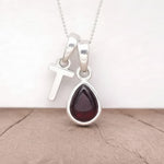 Silver Initial T necklace with a teardrop-shaped Garnet gemstone pendant hanging above a rustic wooden surface