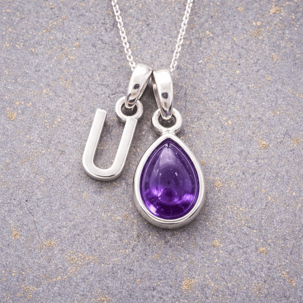Sterling Silver necklace with a 'U' initial pendant and a purple teardrop february birthstone amethyst pendant on a textured grey background 