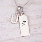 Sterling silver initial U and Sagittarius zodiac bar necklace, close-up of the letter charm and pendant on whitewashed wood