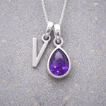 sterling Silver necklace with a 'V' initial pendant and a purple teardrop february birthstone amethyst pendant on a textured grey background