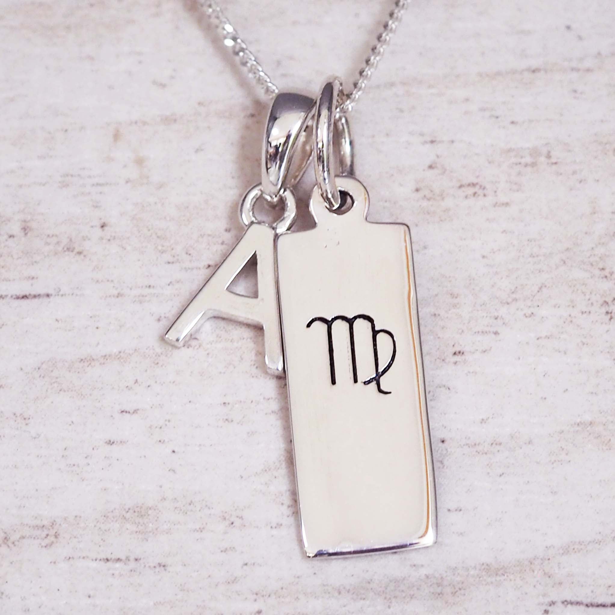 sterling Silver necklace with a rectangle pendant with virgo zodiac glyph, and a 'A' initial pendant on a light background