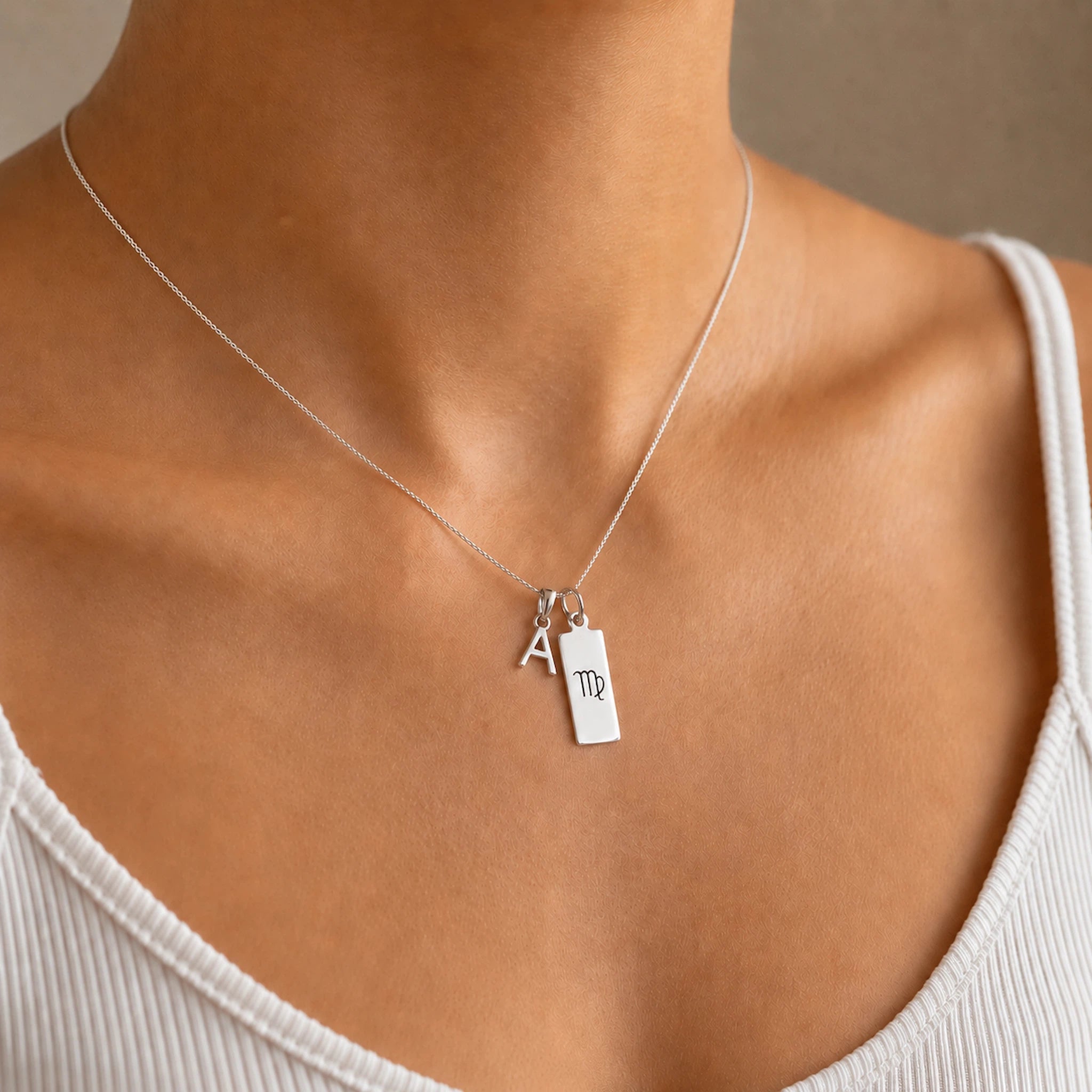 model wearing a sterling silver double pendant Necklace, with a pendant featuring the letter 'A' and a rectangle virgo 'Zodiac' glyph symbol on a person wearing a white tank top.
