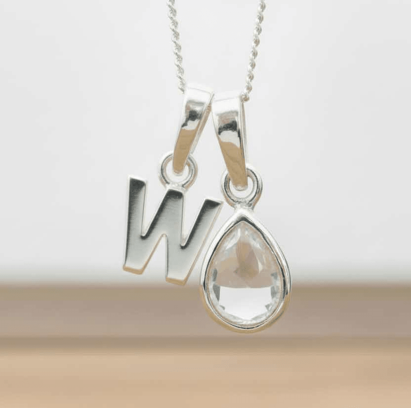 Silver necklace with 'W' pendant and teardrop-shaped herkimer quartz crystal on a neutral background