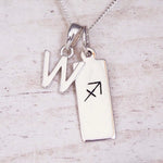 Sterling silver initial W and Sagittarius zodiac bar necklace, close-up of the letter charm and pendant on whitewashed wood