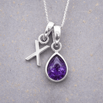 sterling Silver necklace with a 'X' initial pendant and a purple teardrop february birthstone amethyst pendant on a textured grey background