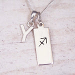 Sterling silver initial Y and Sagittarius zodiac bar necklace, close-up of the letter charm and pendant on whitewashed wood