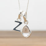 Silver Initial Z necklace with a teardrop-shaped Herkimer Quartz crystal pendant hanging above a rustic wooden surface