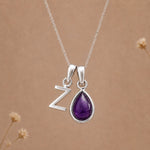 Silver necklace with a teardrop-shaped february birthstone amethyst gemstone pendant and a silver 'Z' charm on a beige background.