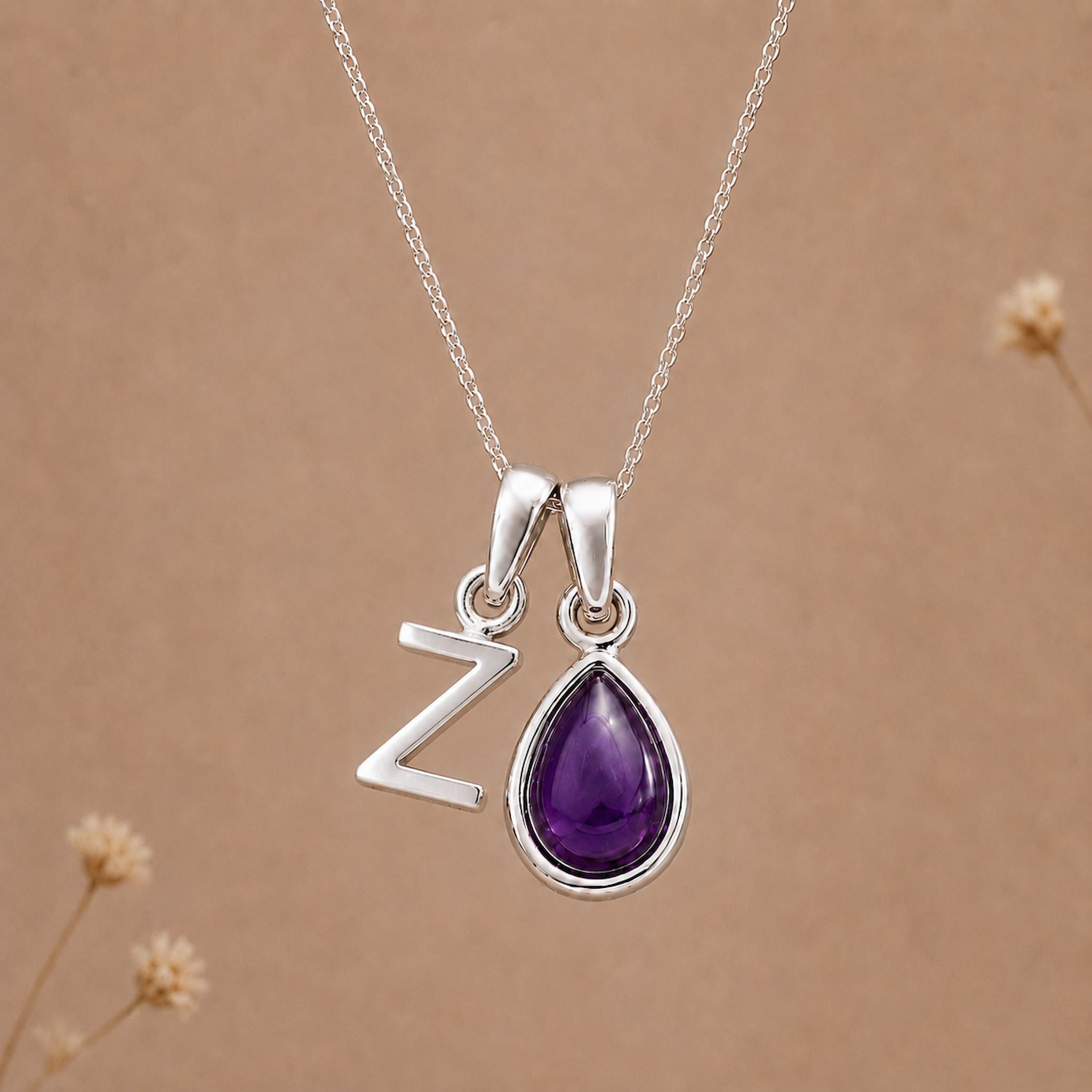 Silver necklace with a teardrop-shaped february birthstone amethyst gemstone pendant and a silver 'Z' charm on a beige background.