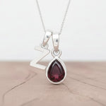 Silver Initial Z necklace with a teardrop-shaped Garnet gemstone pendant hanging above a rustic wooden surface