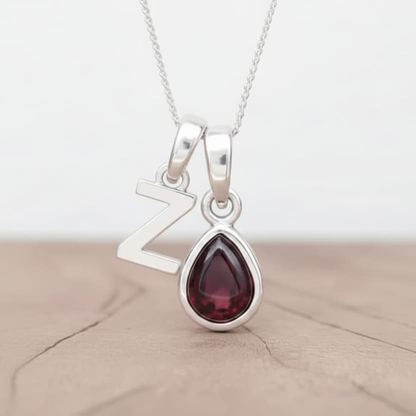 Silver Initial Z necklace with a teardrop-shaped Garnet gemstone pendant hanging above a rustic wooden surface
