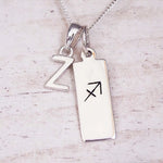 Sterling silver initial Z and Sagittarius zodiac bar necklace, close-up of the letter charm and pendant on whitewashed wood