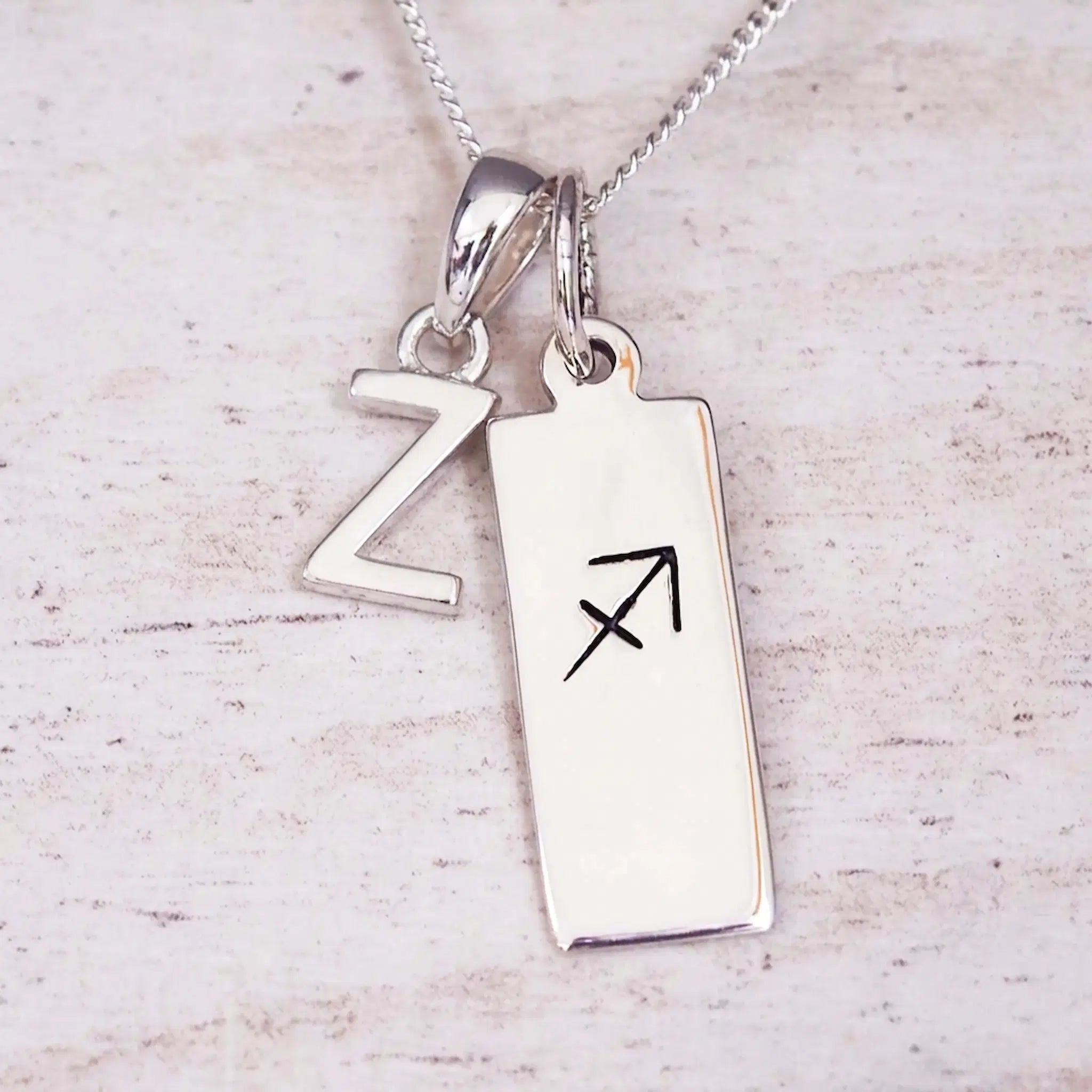 Sterling silver initial Z and Sagittarius zodiac bar necklace, close-up of the letter charm and pendant on whitewashed wood