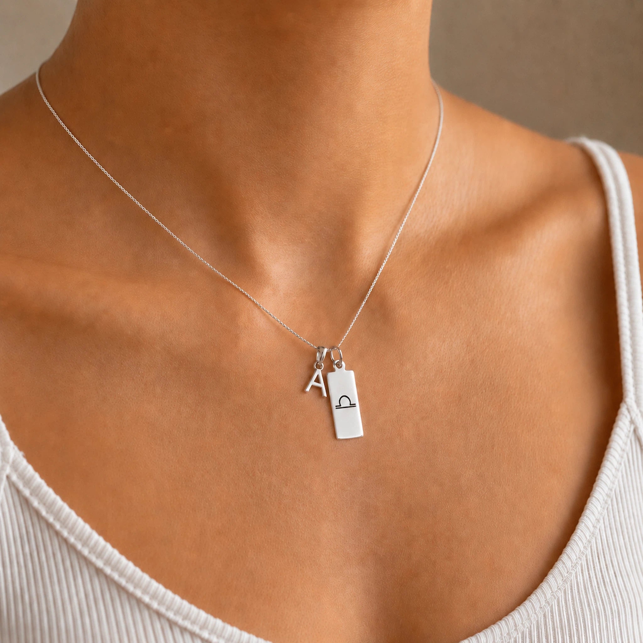 model wearing a sterling silver necklace with a upper case block letter pendant and a rectangle pendant with zodiac glyph