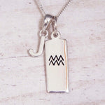 Sterling Silver J Initial and Aquarius Necklace on a fine silver chain against a light wooden background