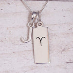 Sterling Silver J Initial pendant and Aries necklace on a fine silver chain on a light wooden background