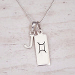 Sterling silver J initial and GeminI Necklace on a fine silver chain on a light wooden background
