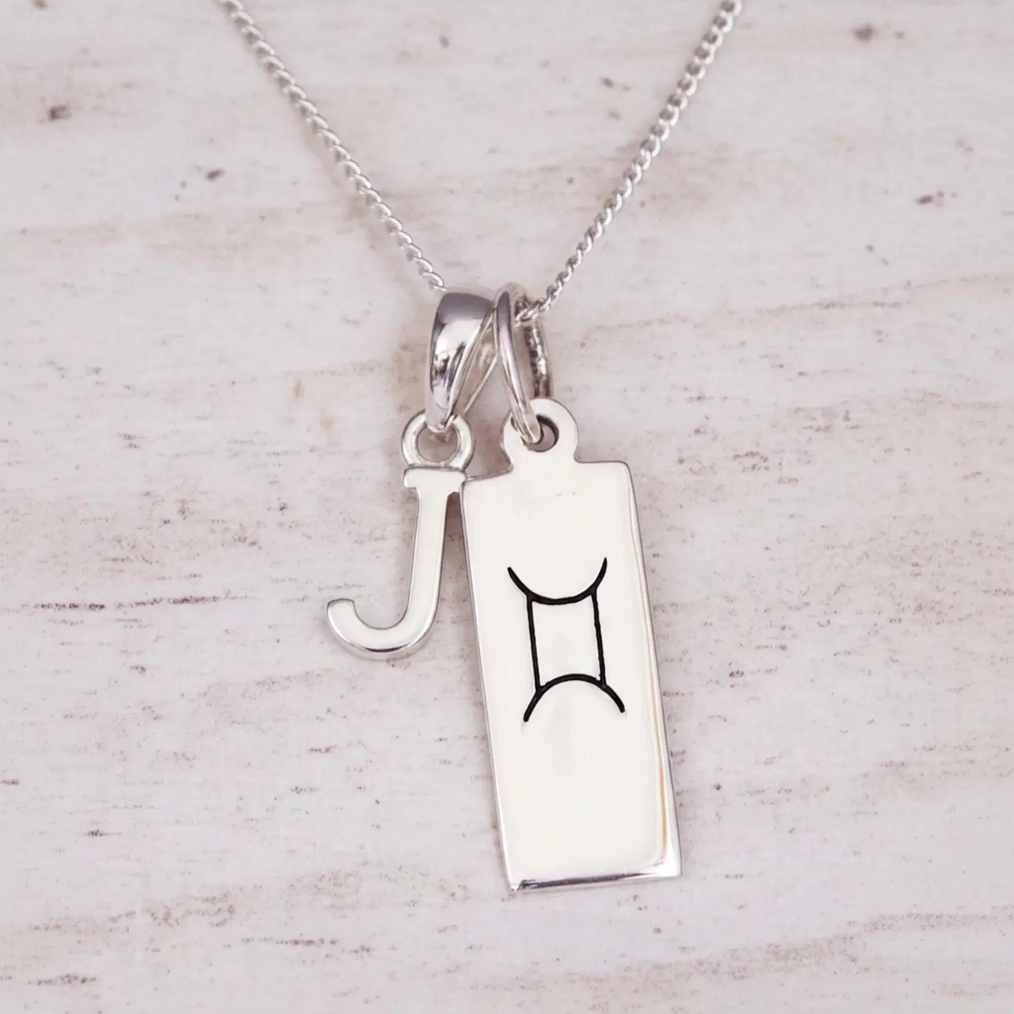 Sterling silver J initial and GeminI Necklace on a fine silver chain on a light wooden background