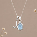 Sterling silver initial J and November natural blue topaz necklace on a taupe background with sparse ivory flowers