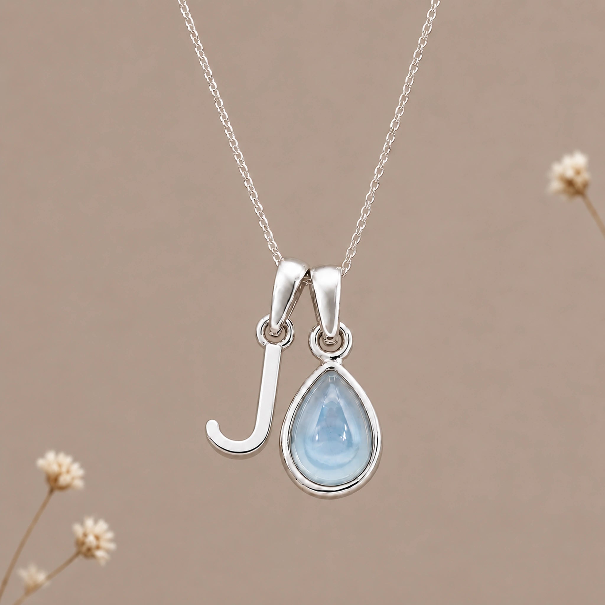 Sterling silver initial J and November natural blue topaz necklace on a taupe background with sparse ivory flowers