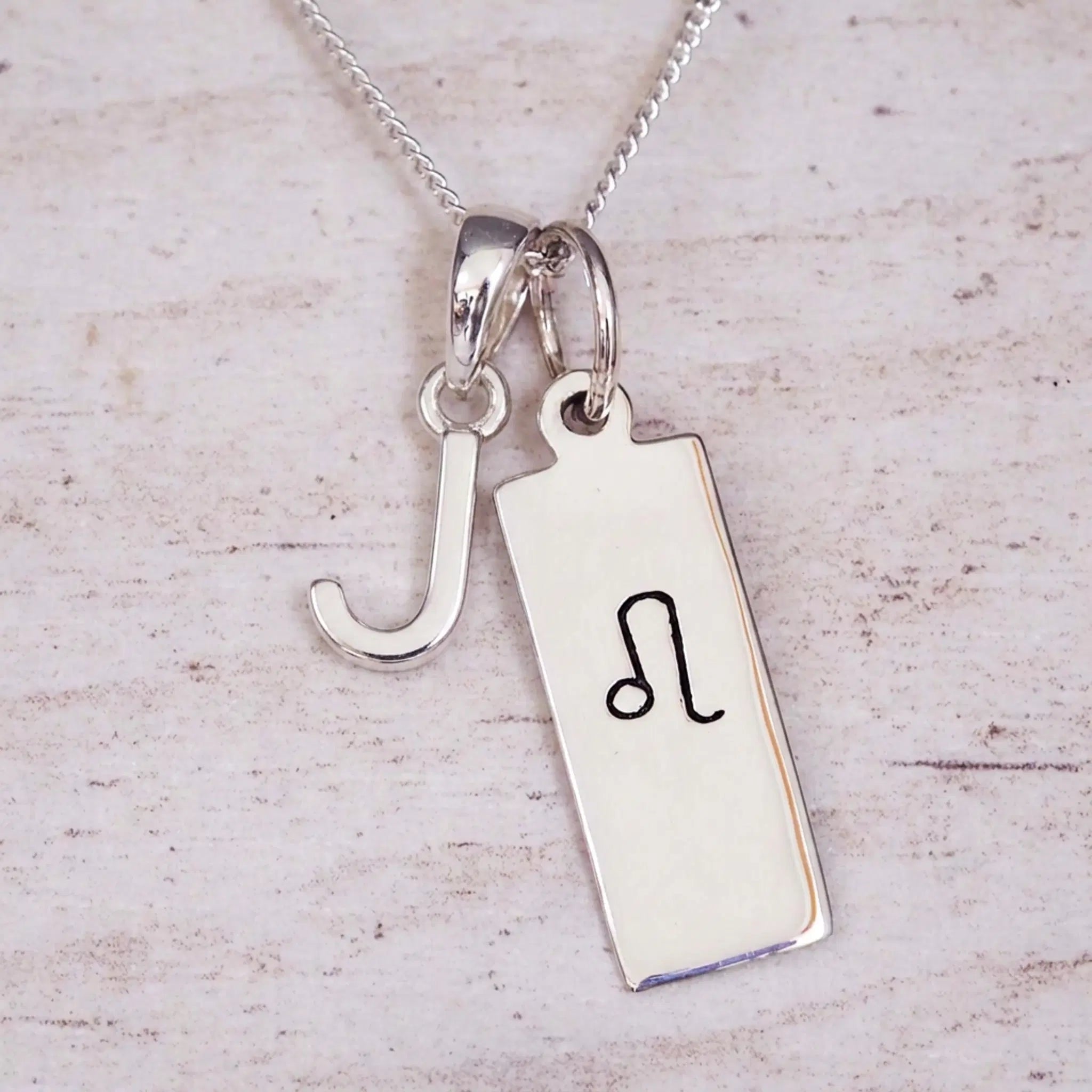 sterling silver initial j leo zodiac star sign pendant necklace against a light wooden background