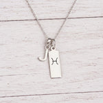 sterling silver J initial Pisces Necklace on a fine silver chain against a light wooden background