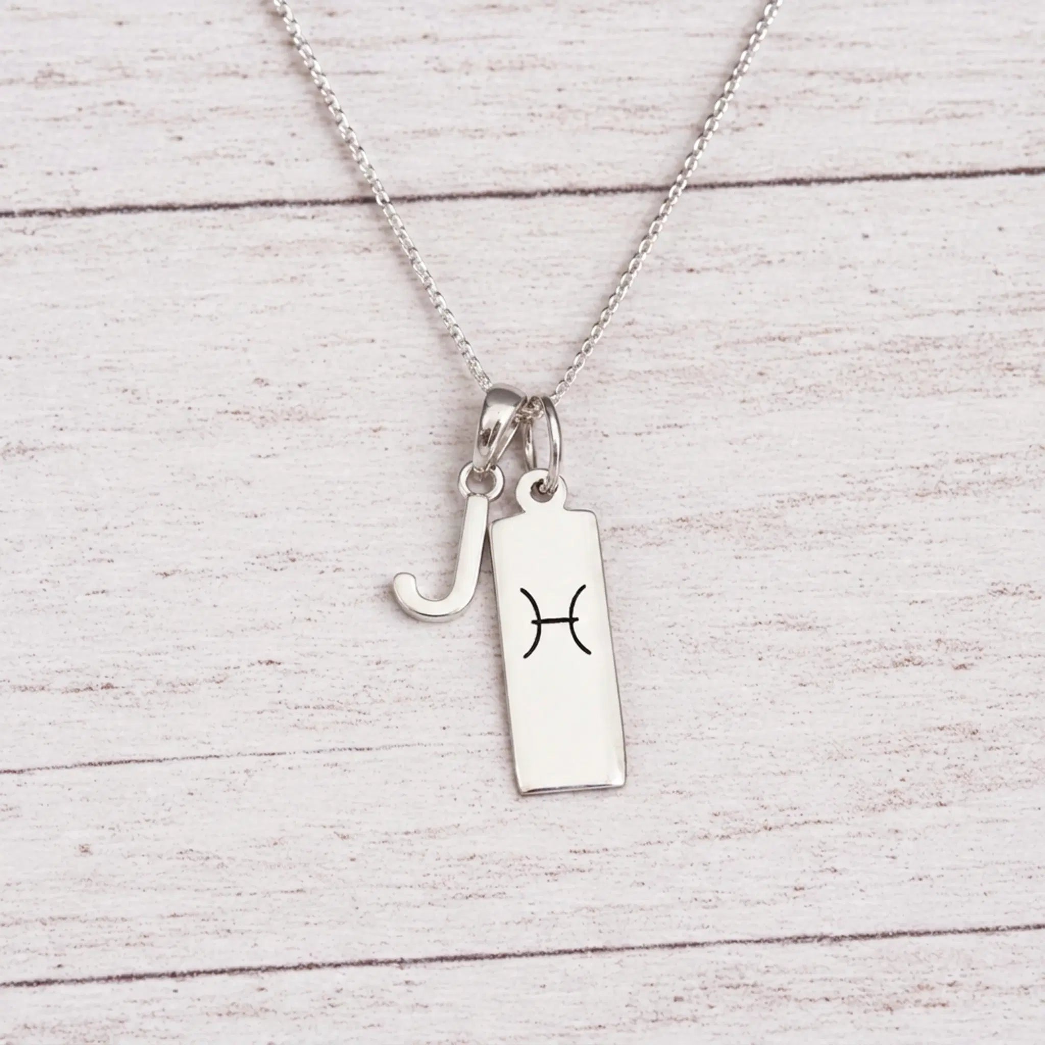 sterling silver J initial Pisces Necklace on a fine silver chain against a light wooden background