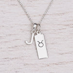 Sterling silver J initial Pendant and Taurus Necklace on a fine silver chain on a light wooden background